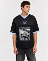 Remera de estilo deportivo con cuello en V y detalles en celeste. Presenta un estampado gráfico central con una escena de fútbol y la frase Sabremos Cumplir.