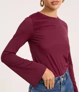 Blusa ajustada de manga larga color marrón, con cuello redondo y fruncido en los hombros y laterales.