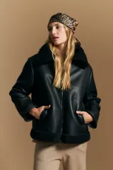 Campera tipo gamulán de cuero sintético negro, con interior y detalles de corderito sintético al tono en cuello y ruedo. Presenta cierre frontal metálico y diseño de silueta relajada.