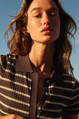 Top de punto confeccionado en mezcla de viscosa, con diseño a rayas horizontales en color marrón y amarillo claro. Presenta cuello polo, manga corta, bajo recto y cierre frontal con botones.