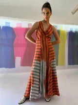 Vestido largo de lino rayado color naranja y marrón, con escote en V y espalda descubierta. La falda es amplia y con mucho movimiento.