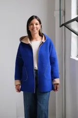 Tapado de paño color azul con capucha, cierre frontal y detalles en color beige en el interior de la capucha, puños y bordes de los bolsillos.