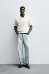 Polo de hombre color blanco hueso, de corte regular fit, con cuello solapa y tapeta de dos botones. Manga corta terminada en rib.