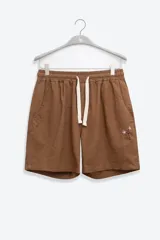 Short de lino color marrón con cintura elástica, cordón de ajuste y bordado floral en la pierna izquierda.
