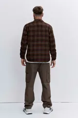 Campera tipo sobrecamisa de franela a cuadros en tonos marrones y verdes, con cuello clásico, cierre frontal de botones y bolsillos con solapa en el pecho.