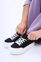 Championes de lona color negro con plataforma de goma blanca y cordones blancos. Presentan ojales metálicos en color cobre.