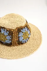 Sombrero de ala ancha color tostado, tejido en papel con detalles de apliques de crochet en la parte central con diseño de flores en tonos celestes, marrones y verde oliva.