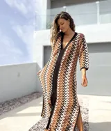 Vestido largo de tejido de punto con diseño geométrico en tonos tierra, negro y blanco. Presenta escote en V profundo, mangas tres cuartos y tajos laterales en la falda.