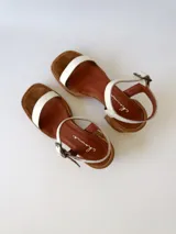 Sandalias de cuero color crudo, con dos tiras anchas sobre el empeine, pulsera al tobillo con hebilla y taco cuadrado de madera.