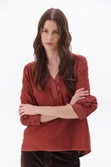 Blusa color ladrillo con escote en V, cuello camisero y mangas largas con puños abotonados.