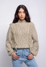 Sweater color crema de tejido trenzado con cuello alto, mangas largas abullonadas y detalle de flecos en el frente.