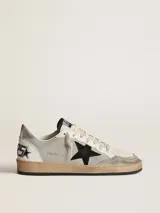 Championes Golden Goose modelo Ball Star, de caña baja, confeccionados en cuero color blanco con detalles en gris y negro. Presentan una estrella negra en el lateral, talón plateado con logo y suela de goma con efecto envejecido.