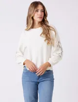 Buzo blanco de modal, corte clásico, con mangas largas abullonadas y apliques de crochet floral en los hombros y parte superior de las mangas.