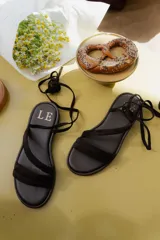 Sandalias planas de cuero con tiras finas que se atan alrededor del tobillo y la pierna. Diseño minimalista con suela flexible y ligera.