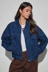 Campera de jean azul oscuro, de corte oversize, con cuello clásico, cierre frontal con cremallera y botones a presión, bolsillos frontales con solapa y mangas largas.