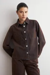 Sobrecamisa de jean efecto terciopelo color marrón con costuras visibles y botones metálicos a presión. Presenta bolsillos frontales con solapa y mangas largas con puños abotonados.