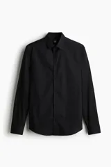Camisa de vestir negra con cuello inglés, tapeta clásica y mangas largas con puños ajustables. Presenta un corte entallado que se ajusta al cuerpo y bajo levemente redondeado.