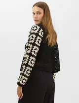 Cardigan abierto de tejido de punto calado con diseño geométrico bicolor en mangas y paneles frontales, y espalda en tono sólido. Presenta silueta recta, frente abierto sin cierre y terminaciones con vivos reforzados en escote, puños y ruedo.