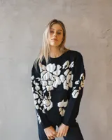 Sweater de tejido de punto en color negro con diseño floral en contraste blanco, de corte holgado y cuello redondo.