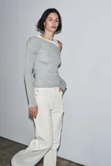 Camiseta de manga larga gris melange con cuello redondo y diseño asimétrico que simula una doble camiseta, con una capa inferior blanca visible en el cuello y el bajo.