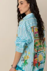 Camisa de manga larga con estampado tropical, fondo a rayas celestes y blancas, cuello camisero y cierre frontal de botones.