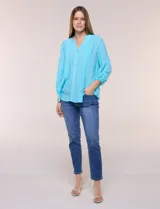 Blusa celeste de silueta suelta y textura liviana, con escote en V, cuello mao y cierre frontal de botones. Cuenta con alforzas verticales en el pecho y mangas tres cuartos con puños elastizados y detalle de galón calado.
