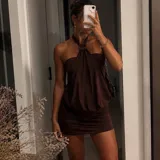 Vestido corto color marrón con diseño de cuello halter, caracterizado por un detalle de argolla circular en el centro del escote y una caída fluida y drapeada en la parte superior, contrastando con una falda ajustada.