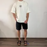 Remera negra de algodón pesado, corte oversize, con un gran estampado en la espalda en blanco y negro que muestra la parte inferior del rostro de una persona con un gorro tejido cubriendo los ojos y un cigarrillo en la boca.