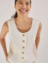 Chaleco sin mangas de lino, con diseño de paneles en color blanco crudo y beige. Presenta escote redondo y cierre frontal con botones de madera marrones.