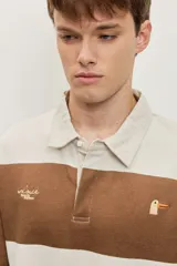 Chomba de friza de manga larga con diseño de rayas horizontales anchas en color beige y azul, cuello polo y pequeño bordado en el pecho.