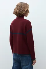 Sweater de punto color crudo con cuello alto y cierre frontal parcial. Presenta detalles de vivos en color marrón en el cuello, hombros y ruedo, con diseño de manga larga.