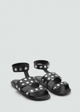Sandalias planas de cuero negro con punta cuadrada, tiras decoradas con tachas metálicas plateadas y tira ajustable al tobillo.