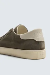 Zapatilla de cordones confeccionada en piel con acabado de serraje. Presenta un diseño liso con detalle de color a contraste en el talón y suela plana de goma a contraste.