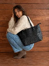Cartera tipo tote bag de cuero vacuno color marrón oscuro, de diseño estructurado con asas largas para llevar al hombro y cierre superior. Presenta detalles de costuras decorativas y pespuntes en el frente.