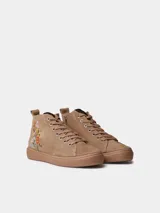 Botín de cuero serraje color beige, con cordones y detalle de flores bordadas en el lateral. Cuenta con suela plana de goma y cierre de cremallera lateral.