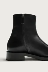 Bota de piel color negro, de caña media, con diseño liso, cierre lateral mediante cremallera, punta afilada y suela con ligero tacón.