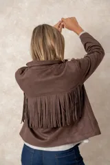 Chaqueta de gamuza sintética color marrón, con diseño de flecos en el pecho y la espalda. Presenta cierre frontal con botones, cuello camisero y bolsillos cuadrados frontales.
