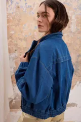 Chaqueta de jean azul con cierre y bolsillos laterales. Cuello alto y puños elastizados. Corte holgado.