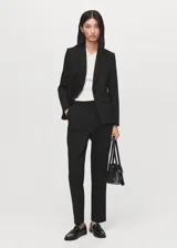 Blazer negro de corte entallado, con cuello de solapa con muesca, hombros estructurados, cierre frontal de un botón, bolsillos de ribete delanteros y manga larga.