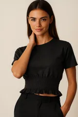 Remera cropped de manga corta, color negro, con cuello redondo y sección inferior con smock elástico que termina en un pequeño volante.