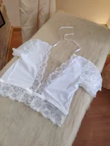 Top blanco de encaje con escote profundo en V, mangas cortas de encaje y detalle de puntilla en el ruedo. Cuenta con tiras finas para atar al cuello.