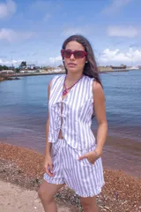 Conjunto de dos piezas compuesto por un chaleco sin mangas con cierre frontal de lazos y un short con volados en el ruedo, ambos con estampado de rayas verticales en tonos blanco y gris.