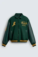 Cazadora estilo varsity con cuerpo de mezcla de lana en color verde oscuro y mangas de efecto piel a tono. Presenta cuello solapa, cierre frontal con botones a presión, bolsillos laterales de vivo y puños y bajo acanalados con rayas amarillas. Incluye bordados y parches decorativos en el frente con la inscripción Boston Archive.