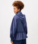 Campera cortaviento de poliéster color azul, con diseño peplum en la cintura, capucha ajustable con cordones y cierre frontal. Presenta mangas largas y un corte funcional y liviano.