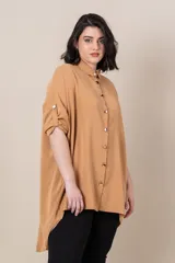 Camisa larga color camel, de corte irregular, más larga en la parte trasera, con botones dorados, manga larga con presilla para sujetar.