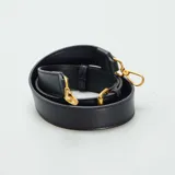 Bolso bandolera negro de cuero con correa ajustable y cierre dorado.