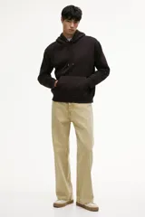 Canguro color marrón oscuro, de corte holgado, con capucha forrada y cordón ajustable. Presenta hombros caídos, bolsillo canguro y remates acanalados en puños y bajo.