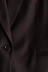 Blazer de botonadura sencilla color marrón oscuro con solapas de muesca, cierre de un botón, hombreras y bolsillos delanteros ribeteados.