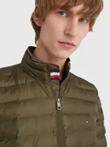 Campera acolchada verde oliva de poliéster reciclado, repelente al agua y plegable. Tiene cierre de cremallera, cuello alto con detalle de la bandera de la marca y logo bordado en el pecho.