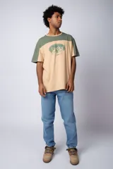 Remera de corte holgado con diseño color block, combinando paneles en color verde menta y blanco. Presenta un estampado frontal con la palabra 'Lucky' dentro de un óvalo y dibujos de flores con lentes de sol.